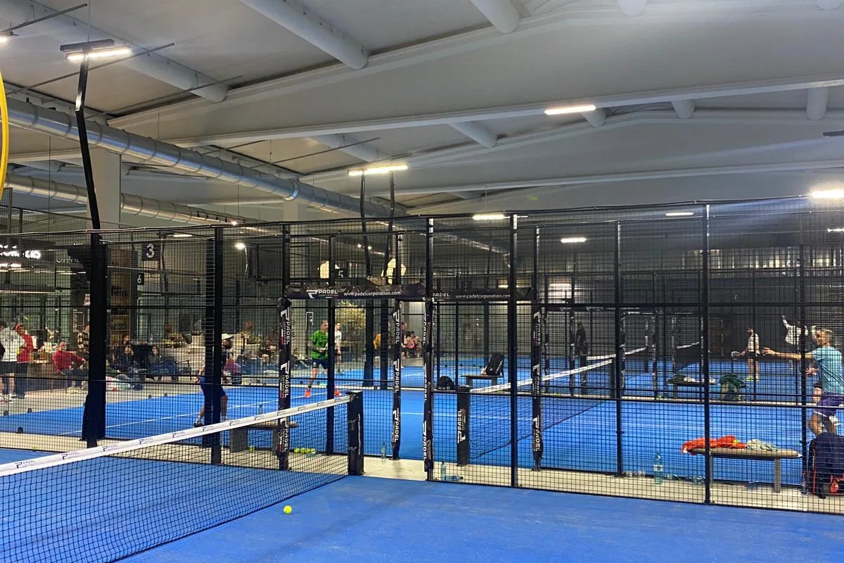 Teren de padel văzut de la fileu, cu jucători pe terenurile din spate
